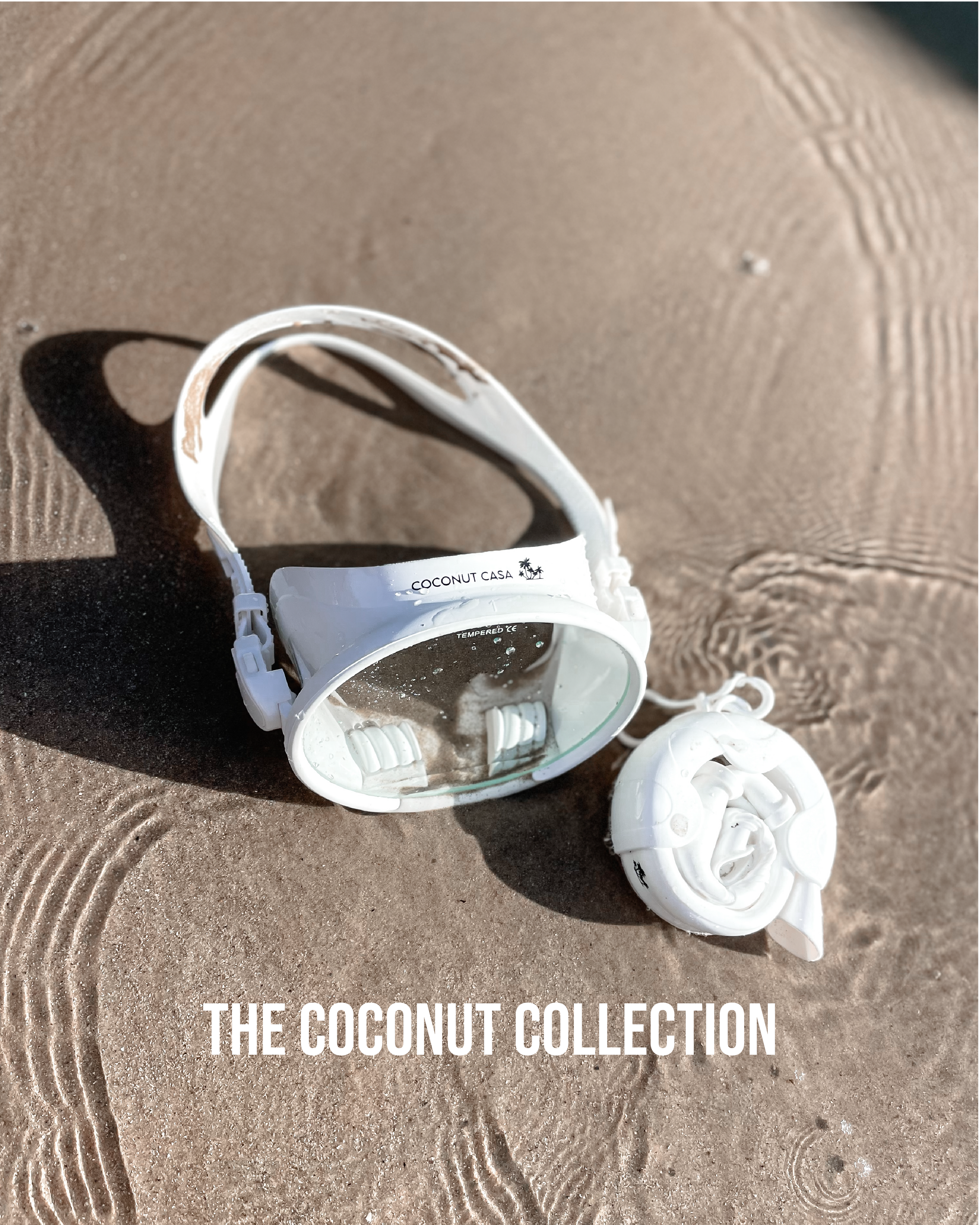 Image of white snorkel set with vintage style mask on the sand in shallow water with the title 'The Coconut Collection' at the bottom
