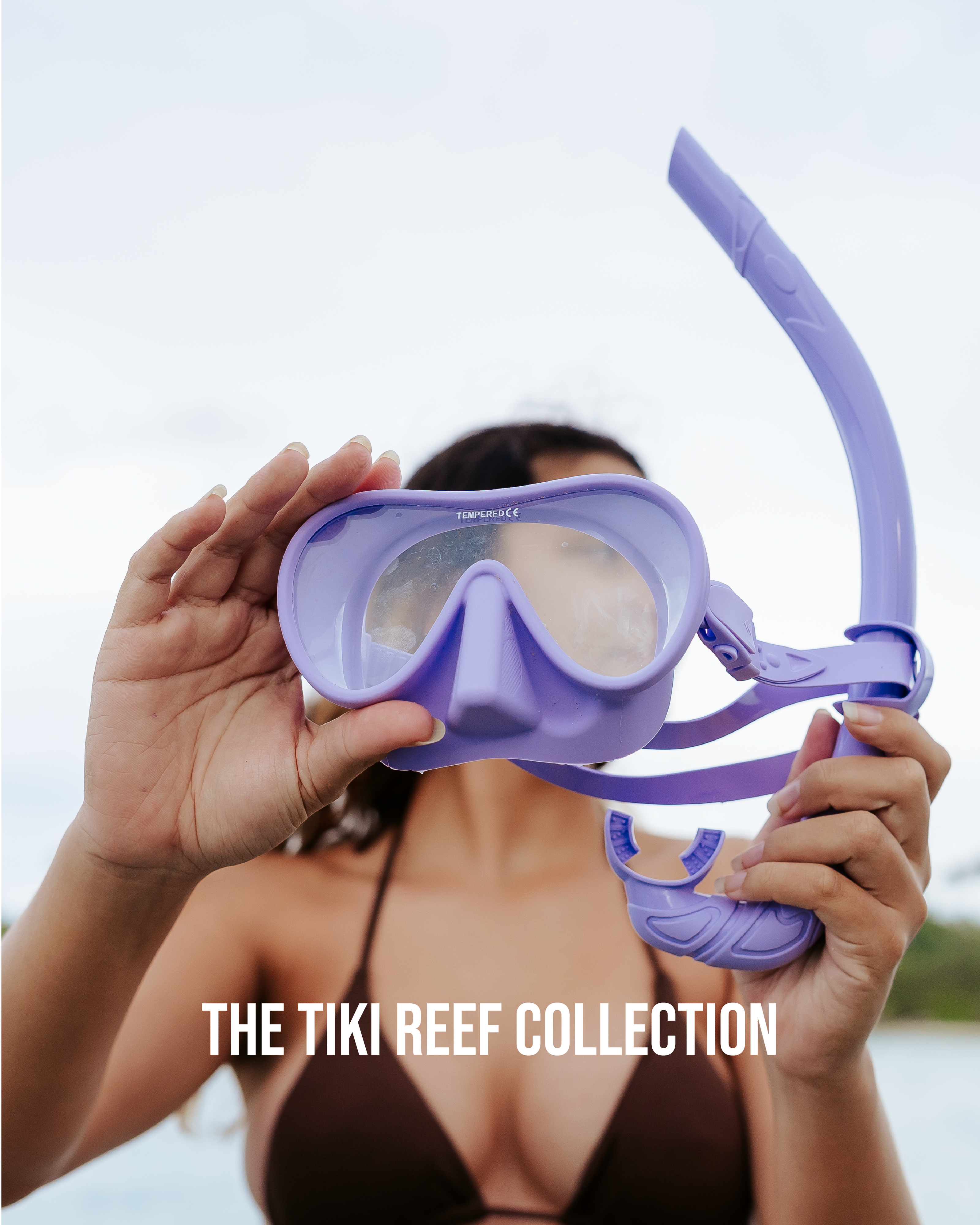 Image of a woman wearing a brown bikini holding a purple snorkel set up to the camera, with the title 'The Tiki Reef Collection' at the bottom